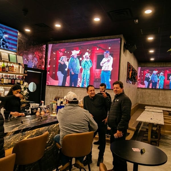 A lively bar scene with patrons, bartenders, and large screens displaying entertainment and news.